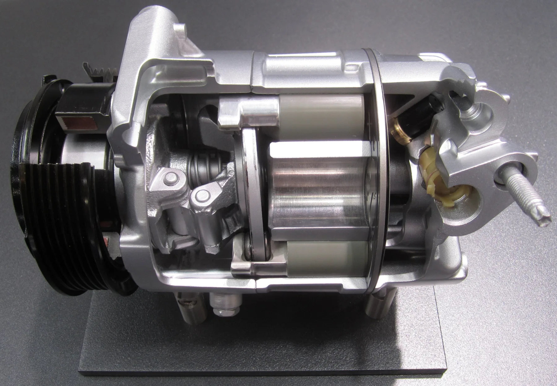 Cutaway of an automotive swash-plate air-conditioning compressor, with the belt pulley, magnetic clutch, tilted plate, pistons, and valve plate