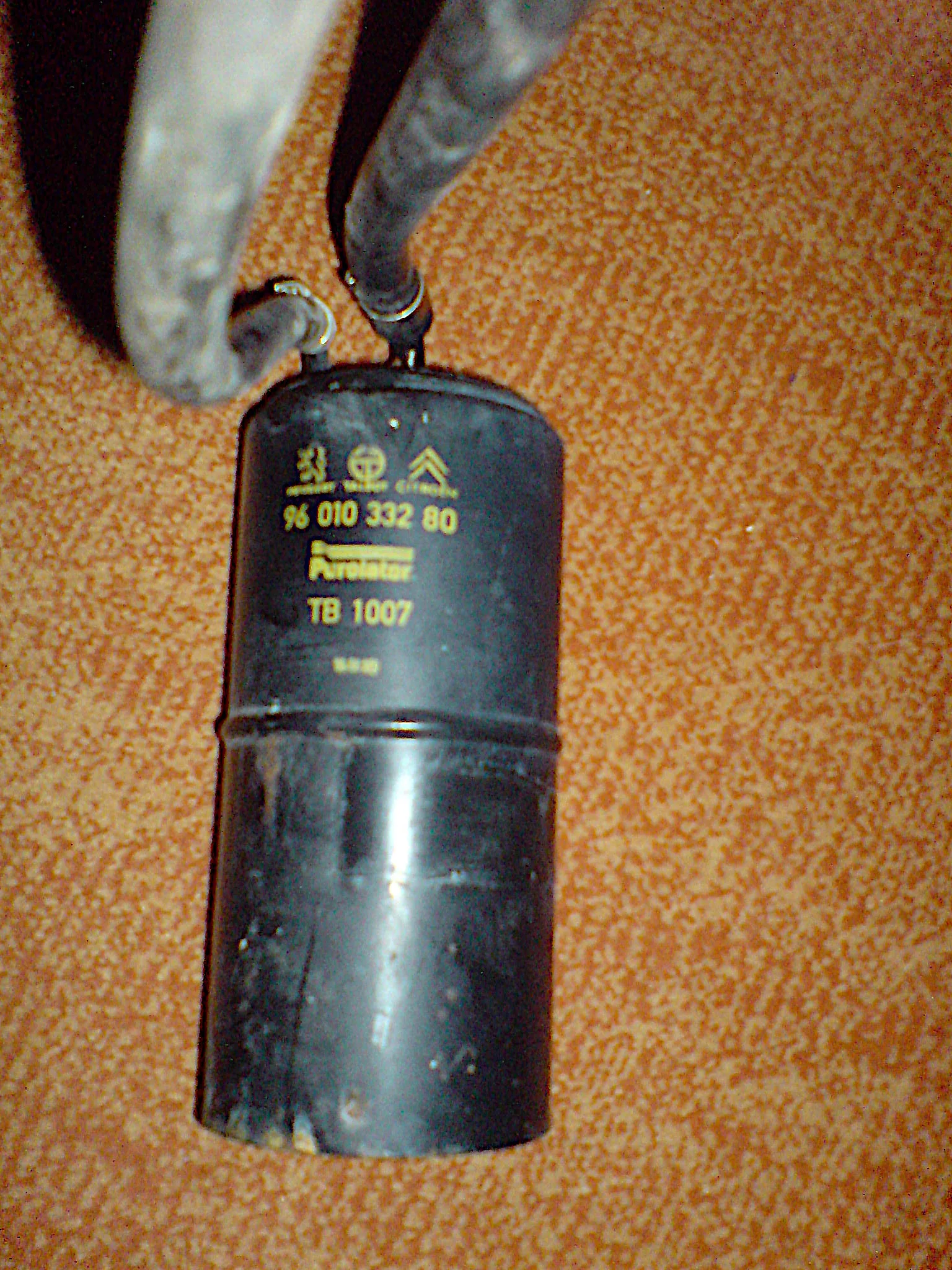 Black cylindrical canister on orange carpet, two hoses clamped to the top, yellow print with Peugeot, Talbot, and Citroën logos, part number 96 010 332 80, Purolator, and TB 1007