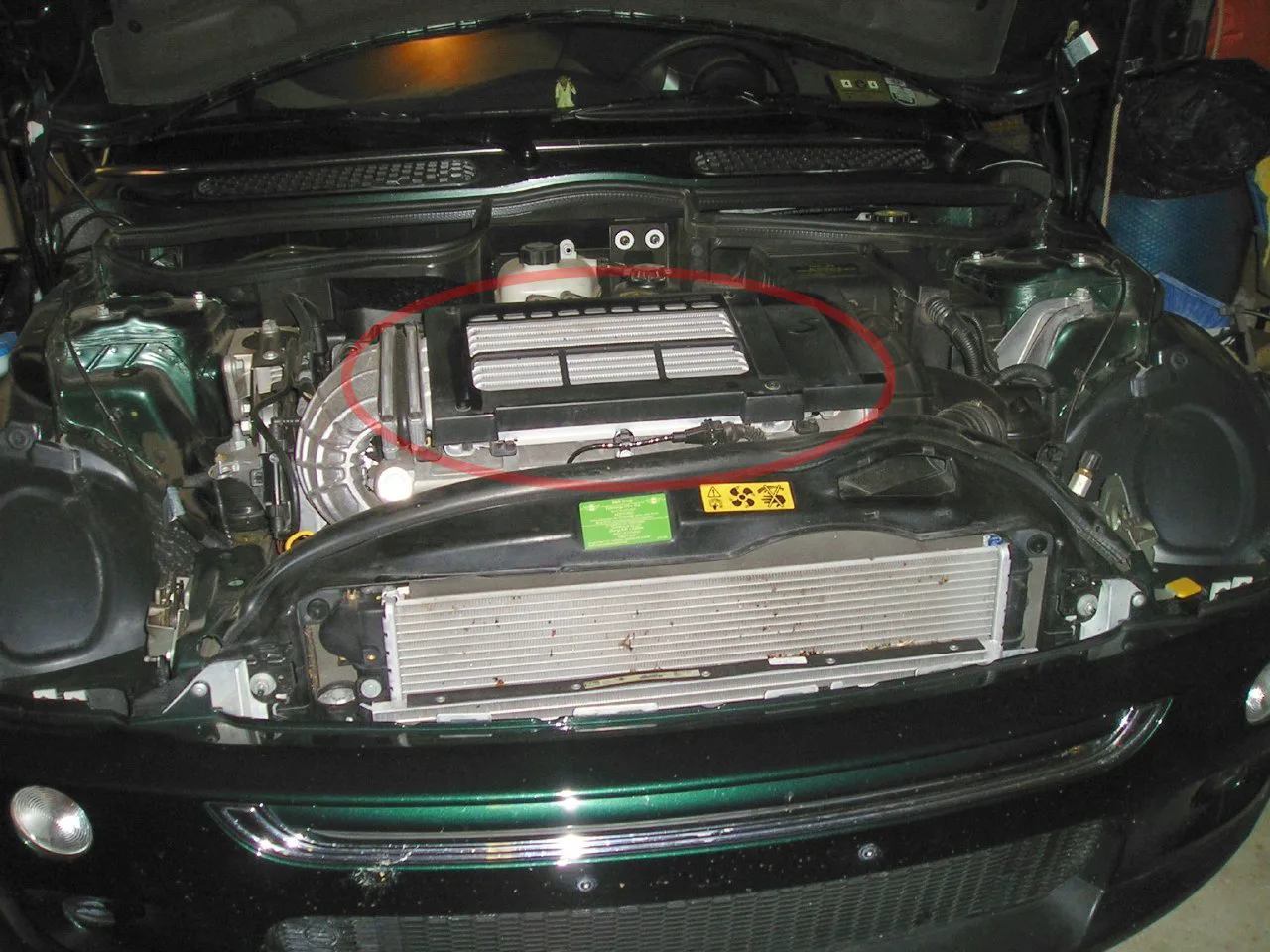 Silver finned top-mount intercooler on a Mini Cooper S engine, above the intake and the belt-driven accessories
