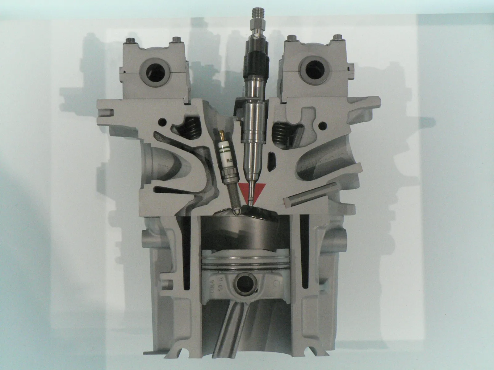 Cylinder-head cutaway showing an injector tip directed into the combustion chamber beside a spark plug