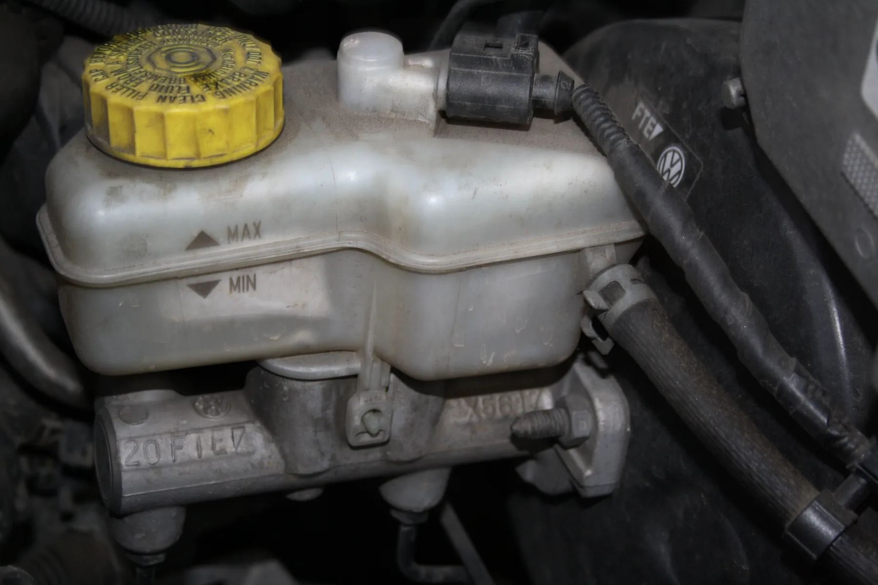 Translucent brake-fluid reservoir with level marks and a yellow cap in an engine bay