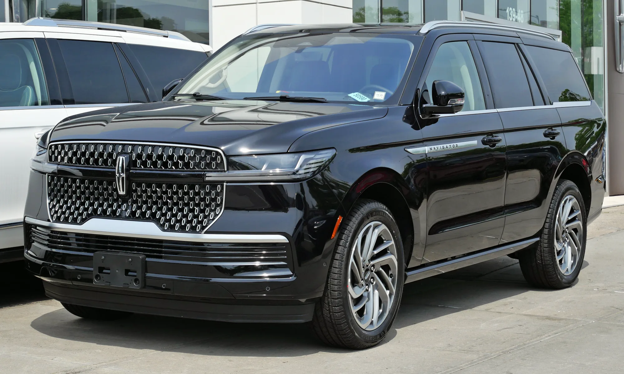 Front three-quarter of a white 2025 Lincoln Navigator with a horizontal light bar across the grille, bright grille slats, and a Lincoln star in the center
