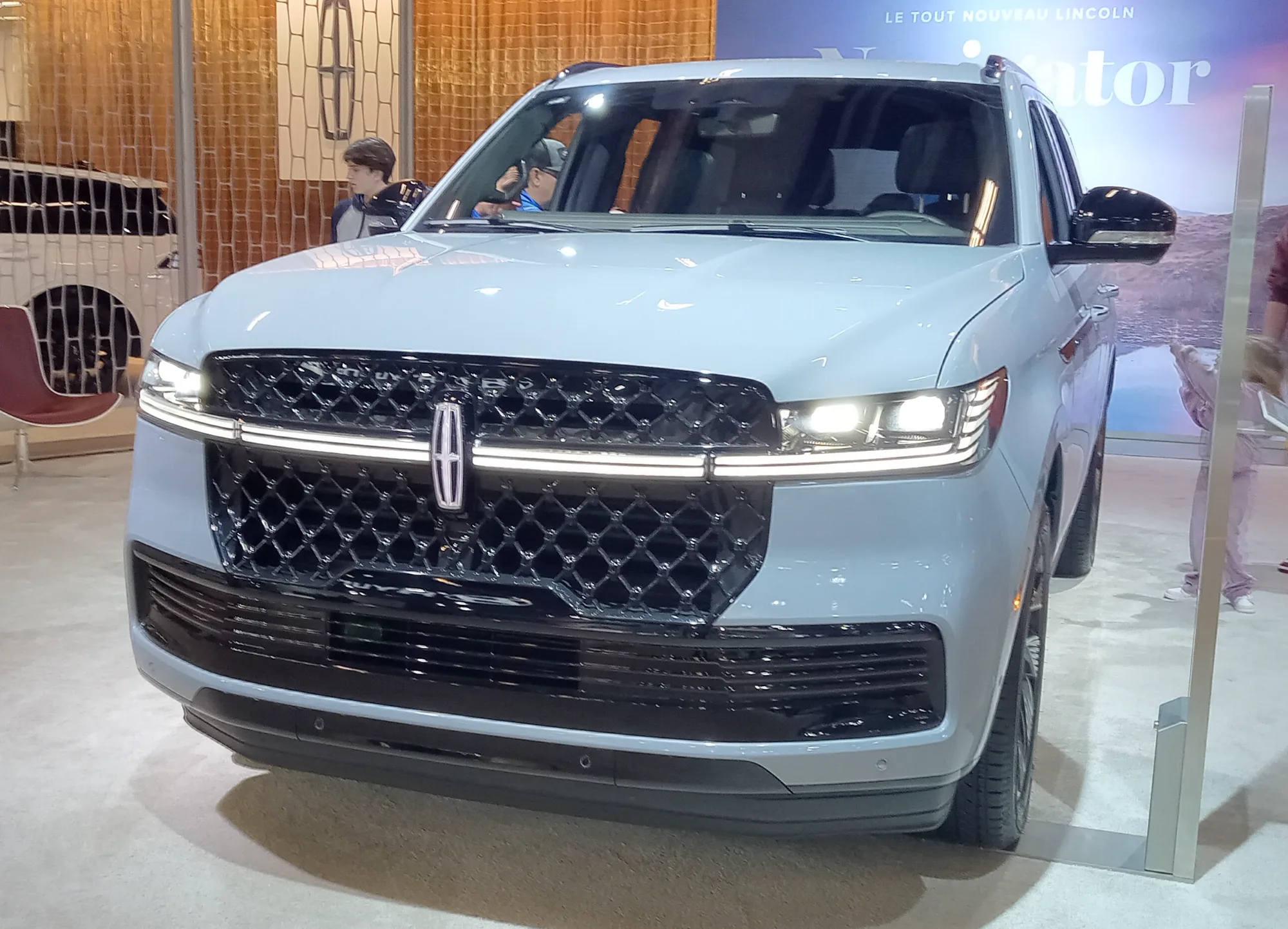 Rear three-quarter of a blue 2025 Lincoln Navigator at an auto show, with a lamp across the tailgate and a Lincoln star centered above it