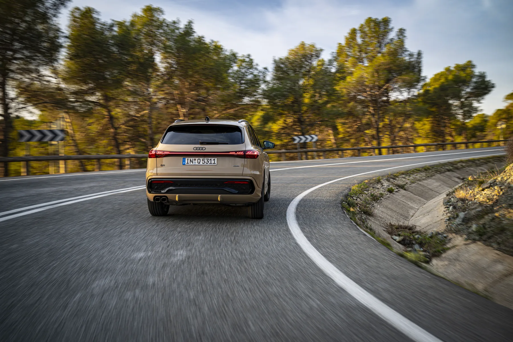 Third-generation Audi Q5 in Sakhir gold, rear three-quarter on a road with a full-width rear light strip