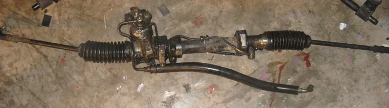 Hydraulic power steering rack with rubber boots, inner tie rods, and hydraulic lines on the housing