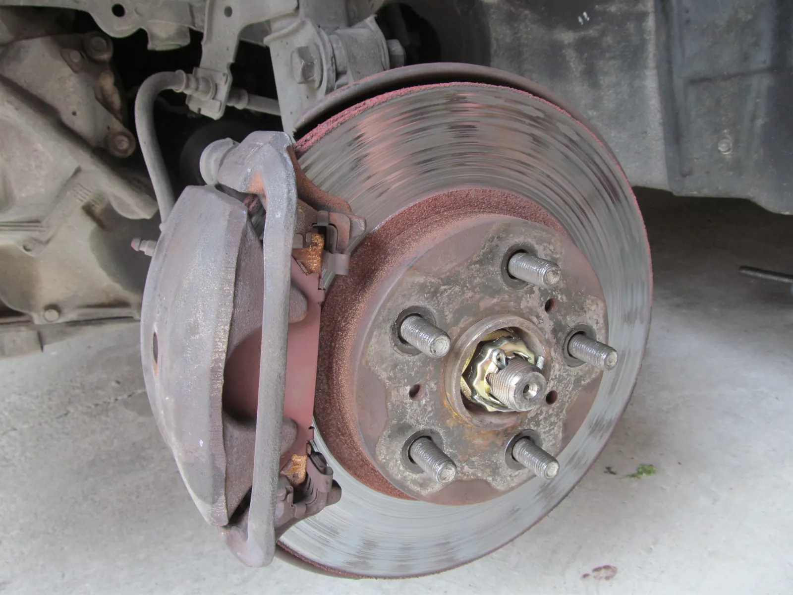 Worn Toyota Corona front brake disc and caliper, with grooves on the disc face