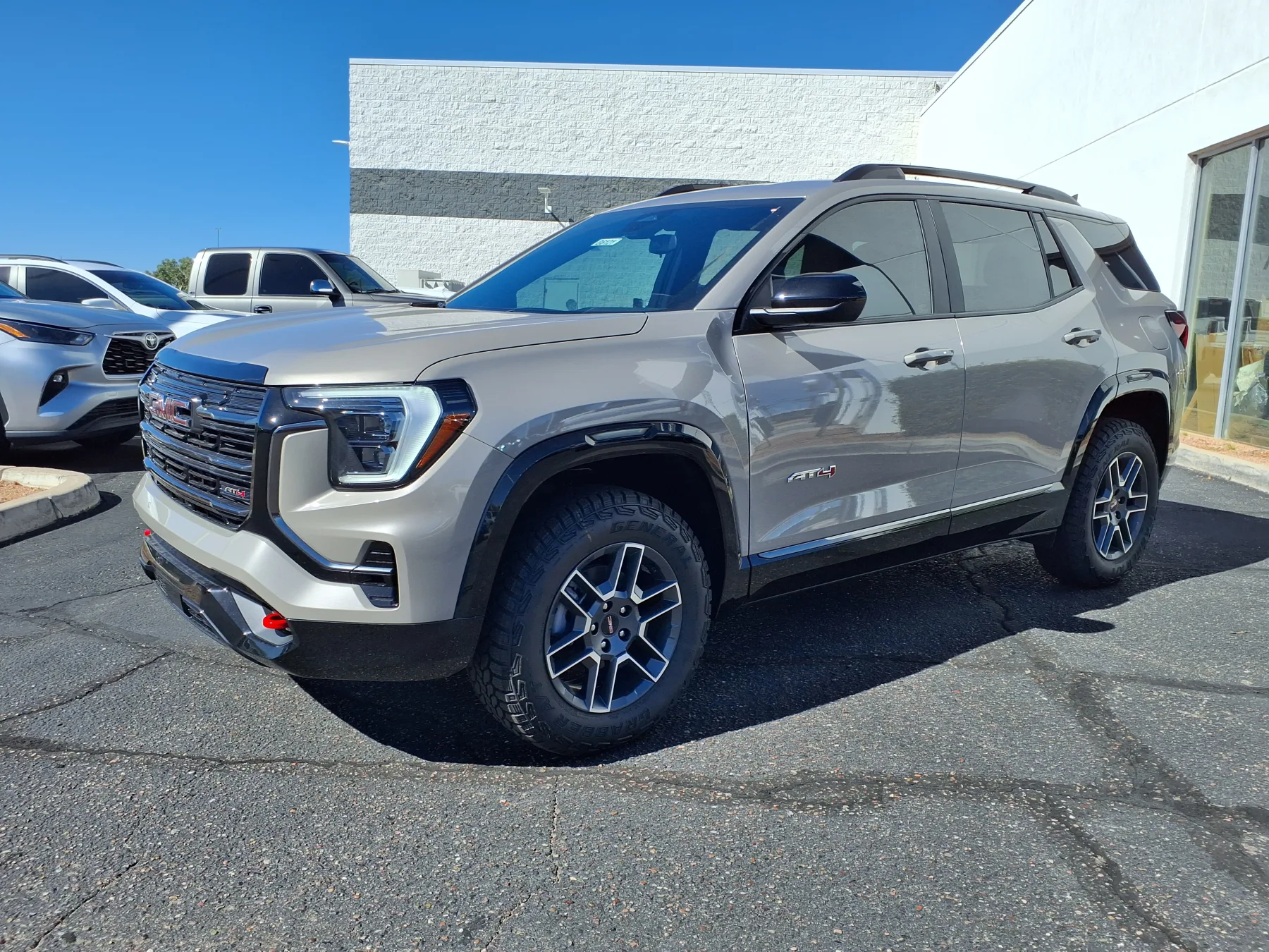 Front three-quarter of a 2026 GMC Terrain AT4 with a bright surround, a dark mesh grille, and red recovery hooks