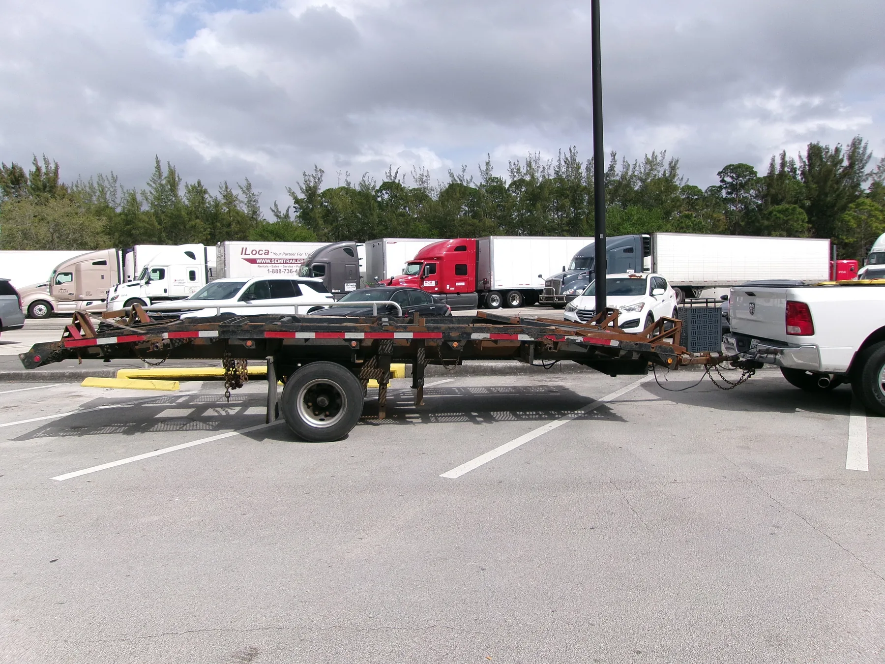 Ram pickup towing a single-axle construction trailer with a ramp in a highway service-plaza lot